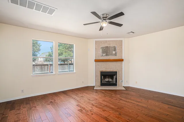 an empty room with wooden floor fireplace and windows