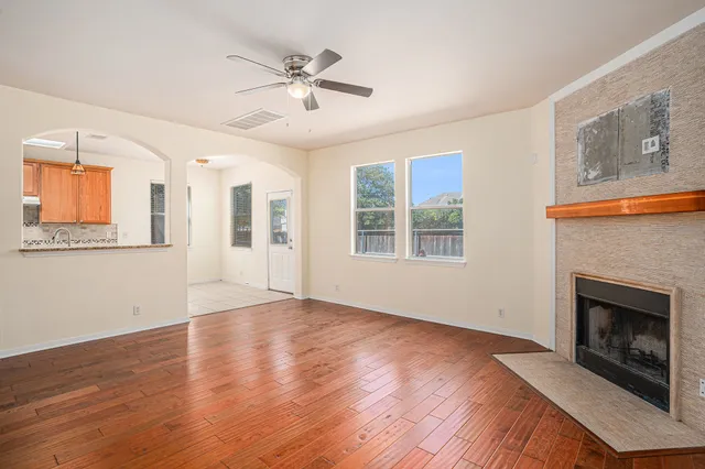 a view of an empty room with wooden floor fireplace and a window
