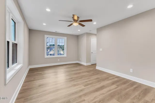 an empty room with wooden floor a ceiling fan and windows