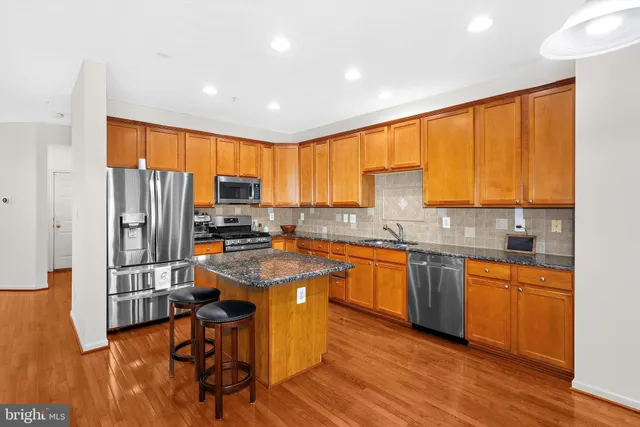 a kitchen with stainless steel appliances granite countertop wooden cabinets a refrigerator a stove a sink and dishwasher with wooden floor