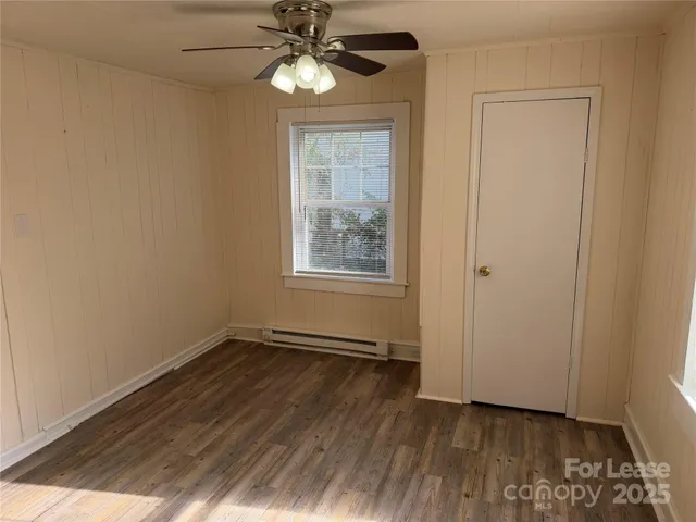 an empty room with wooden floor chandelier fan and windows