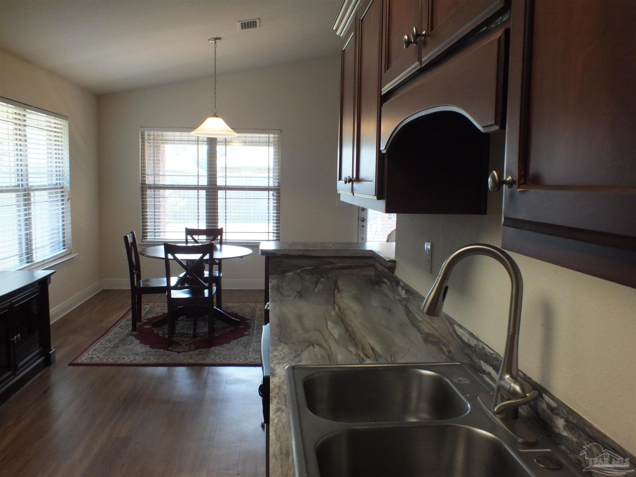 4441 Fiske Street Pace, FL 32571 - Photo 6 of 16 a kitchen with a sink a kitchen island a dining table and chairs with wooden floor