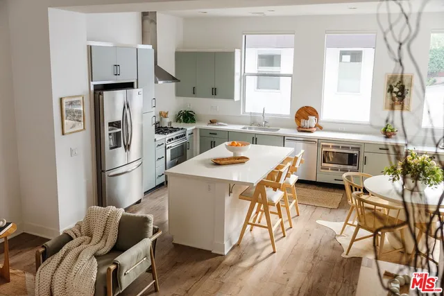 a kitchen with stainless steel appliances granite countertop a dining table chairs refrigerator and sink