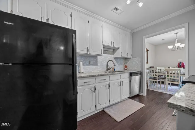 a kitchen with granite countertop a refrigerator stove oven and white cabinets with wooden floor