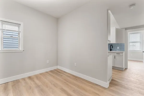 a view of empty room with wooden floor and kitchen