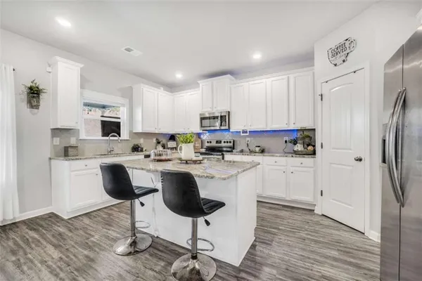 a kitchen with stainless steel appliances granite countertop a refrigerator a stove a sink a microwave and white cabinets with wooden floor