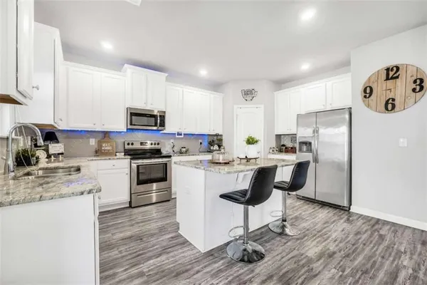 a kitchen with granite countertop a refrigerator a stove a sink a dining table and chairs with wooden floor