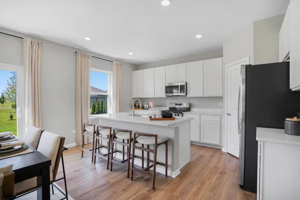 a kitchen with stainless steel appliances a table chairs refrigerator microwave and wooden floor