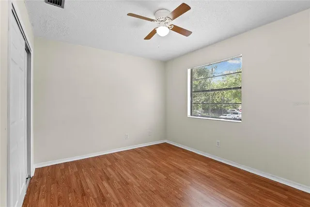 an empty room with wooden floor ceiling fan and windows