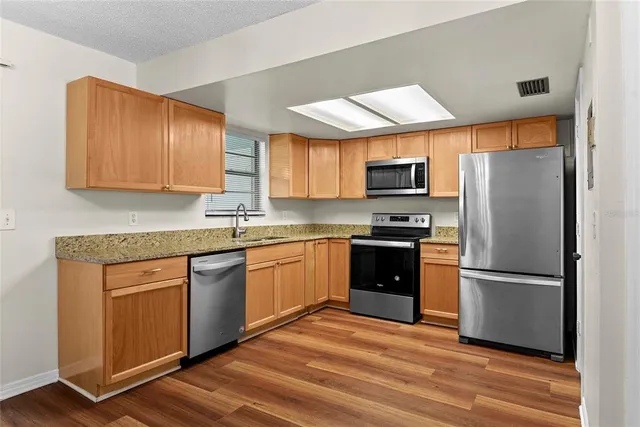 a kitchen with granite countertop wooden floors stainless steel appliances and a sink