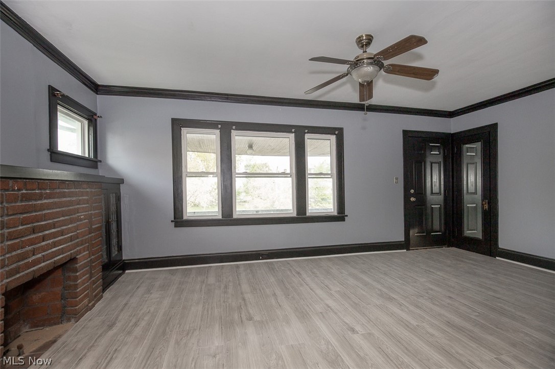 1868-1870 Lampson Road Cleveland, OH 44112 - Photo 5 of 36 Living space with light wood-finish flooring, a brick fireplace, and a ceiling fan with integrated lighting