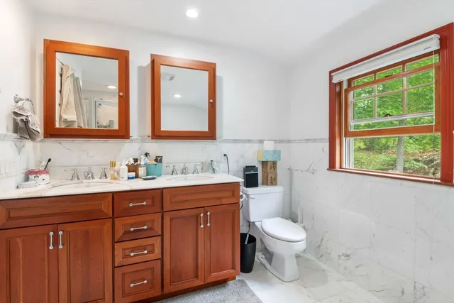 a bathroom with a toilet a sink a mirror a window and vanity