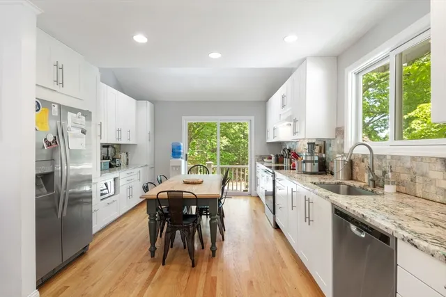 a kitchen with a refrigerator a sink dishwasher a dining table and chairs with wooden floor