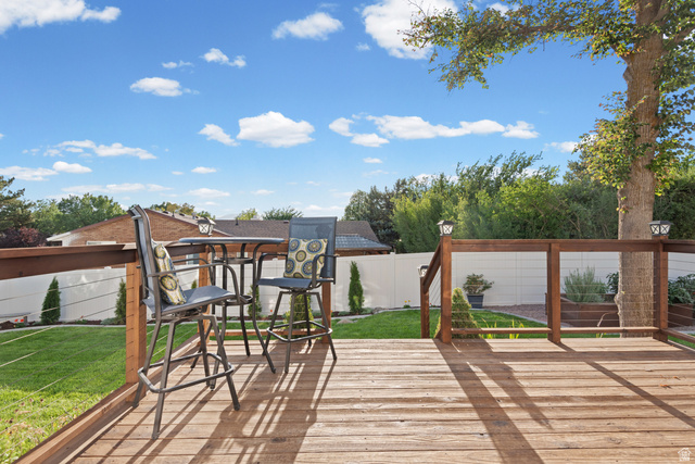 12152 Cinnamon Ridge Road Sandy, UT 84094 - Photo 19 of 34 Expansive composite deck featuring warm wood-finish decking and integrated pergola structure with wooden beams, overlooking a professionally manicured lawn bordered by mature landscaping and privacy fencing
