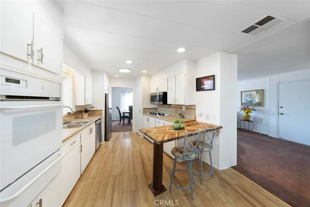 a kitchen with stainless steel appliances granite countertop a stove top oven a sink a dining table and chairs with wooden floor