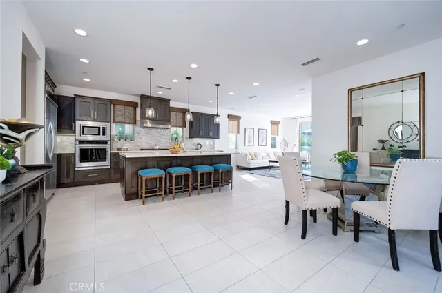 a room with stainless steel appliances kitchen island granite countertop a dining table chairs and a refrigerator