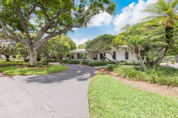 a view of a house with a big yard plants and large trees