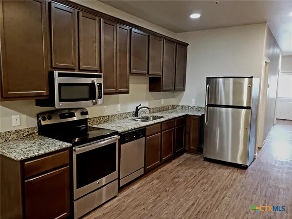 a kitchen with granite countertop wooden cabinets a stove a microwave and a refrigerator