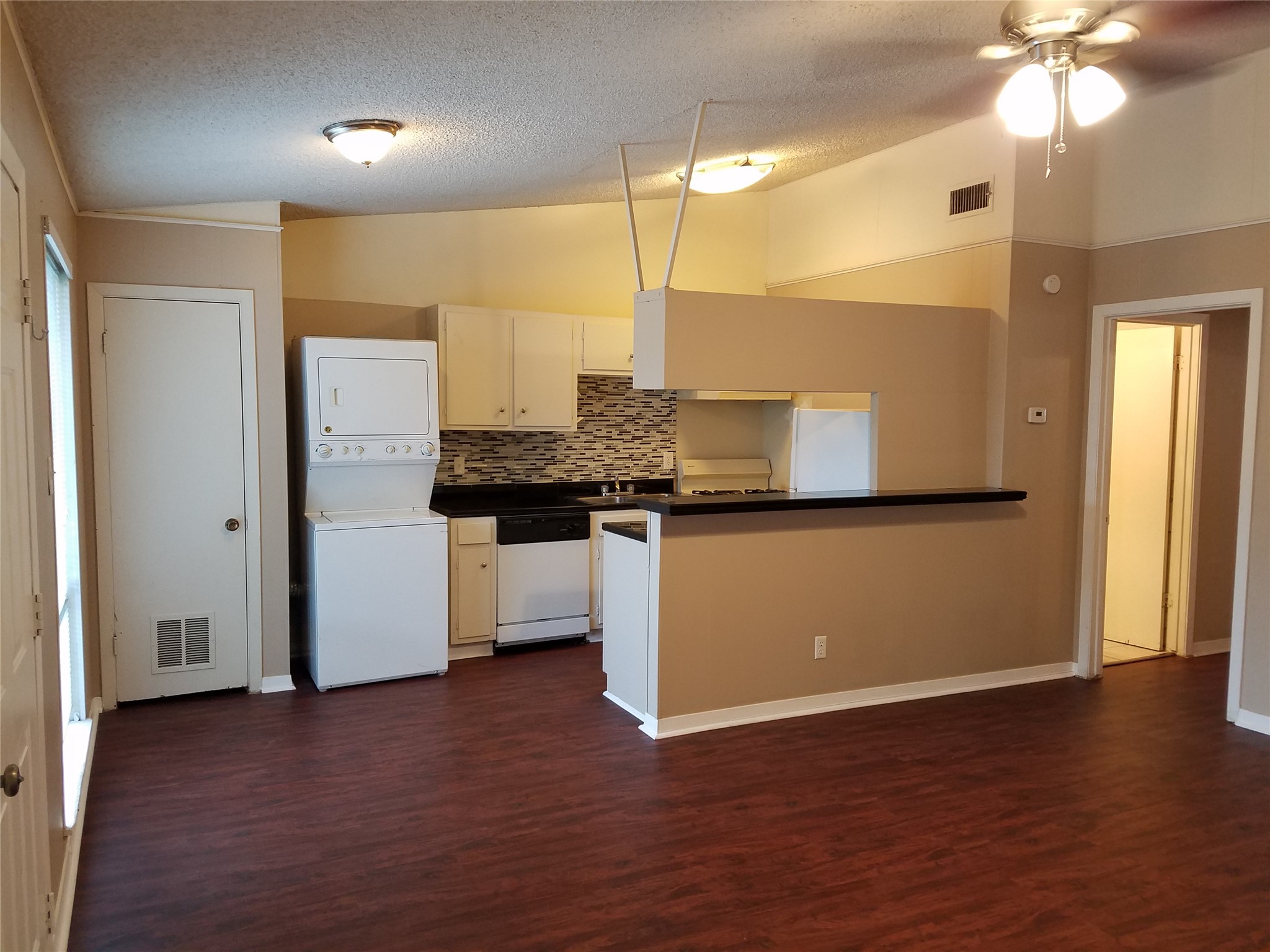 606 West 51st Street, Unit 104 Austin, TX 78751 - Photo 13 of 21 Kitchen featuring dark countertops, tasteful backsplash, dishwasher, stacked washer / dryer, and a ceiling fan