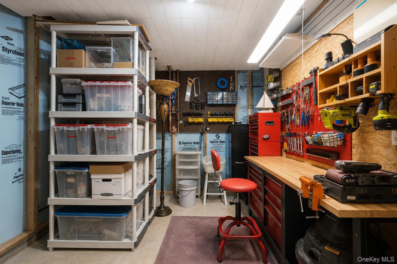 64 Roma Orchard Road Peekskill, NY 10566 - Photo 34 of 40 Utility room featuring extensive built-in shelving, a workbench with a light wood countertop, red storage drawers, a pegboard tool organization system, and overhead fluorescent lighting