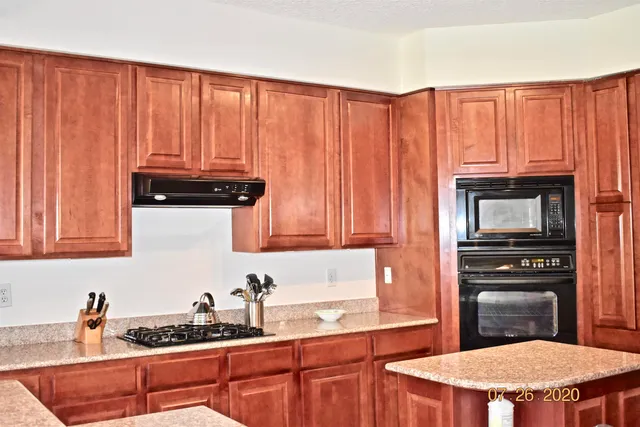 a kitchen with granite countertop wooden cabinets a stove a sink and a microwave
