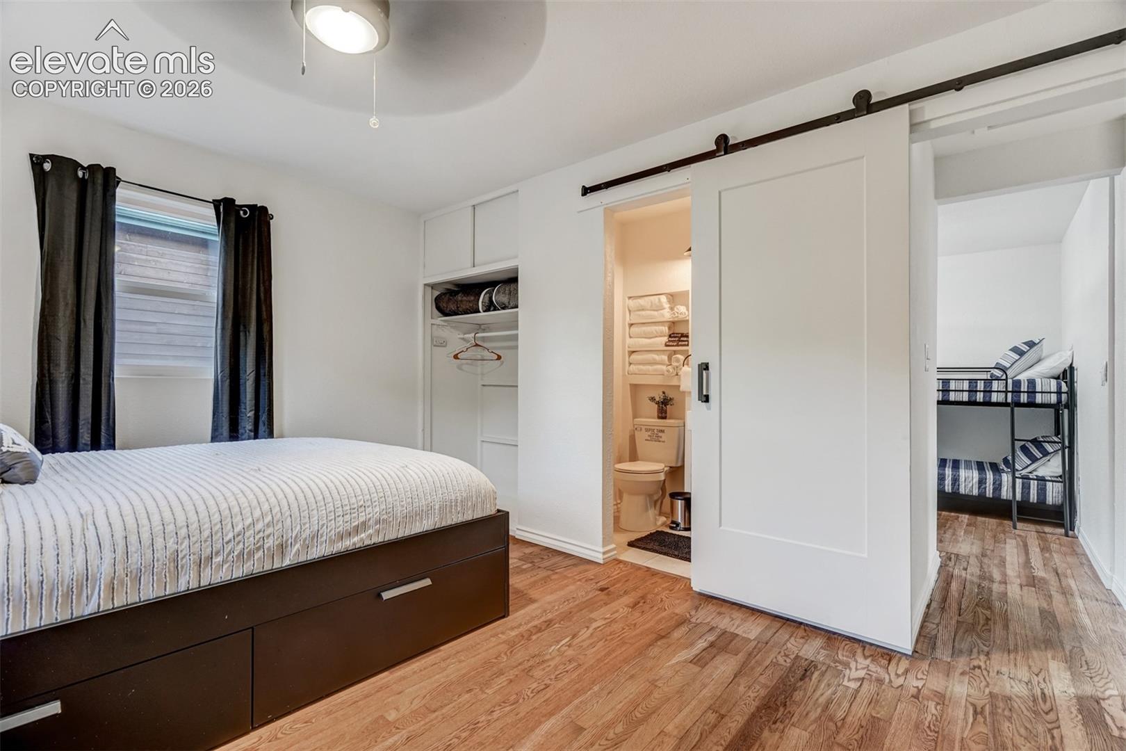 9955 Mesa Road Cascade, CO 80809 - Photo 29 of 41 Wood-finish flooring, built-in storage, modern ceiling fan, white barn door, and a full bathroom with toilet
