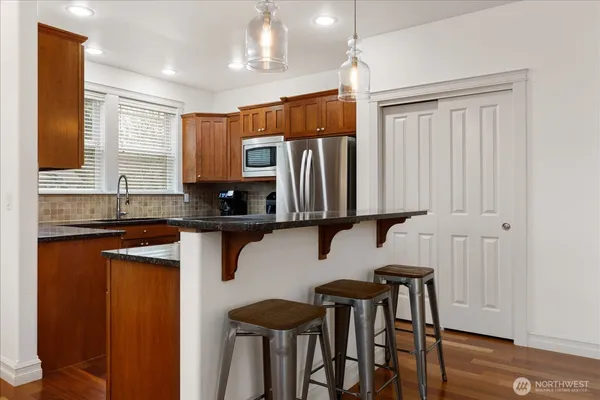 a kitchen with stainless steel appliances granite countertop wooden cabinets a sink a stove a dining table and chairs