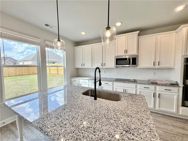 a kitchen with stainless steel appliances granite countertop a sink a stove a refrigerator a microwave oven with white cabinets and wooden floor