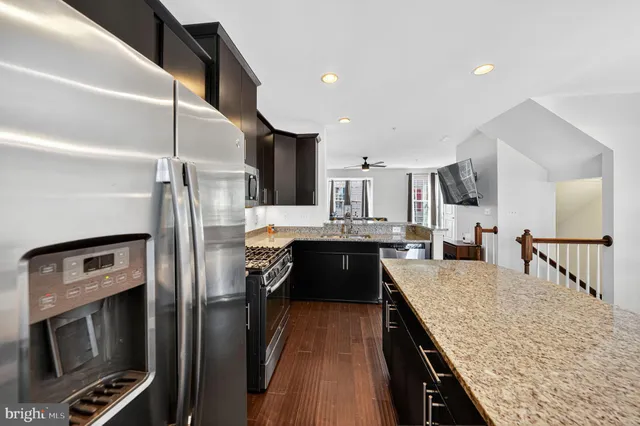 a kitchen with stainless steel appliances granite countertop a refrigerator a stove and a sink with wooden floor