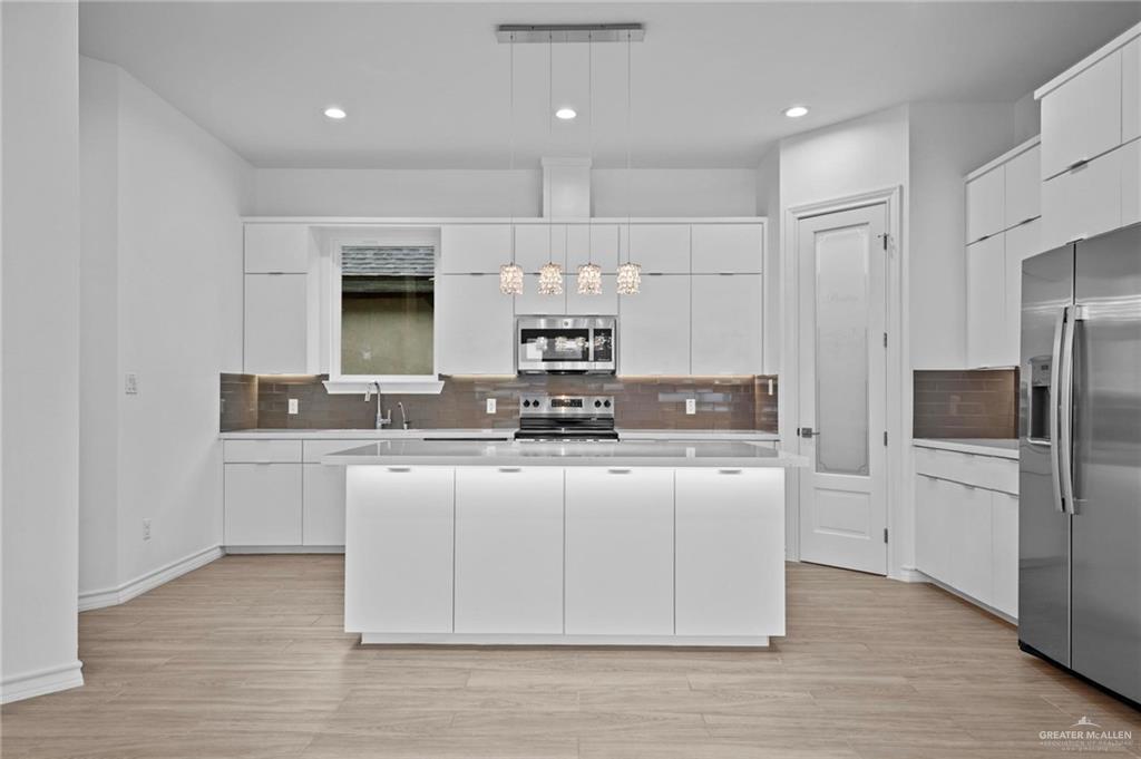 2716 East Conroe Road Edinburg, TX 78542 - Photo 11 of 31 Kitchen featuring pendant lighting, white cabinets, appliances with stainless steel finishes, a center island, and decorative backsplash