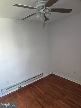 a view of an empty room with wooden floor and a ceiling fan