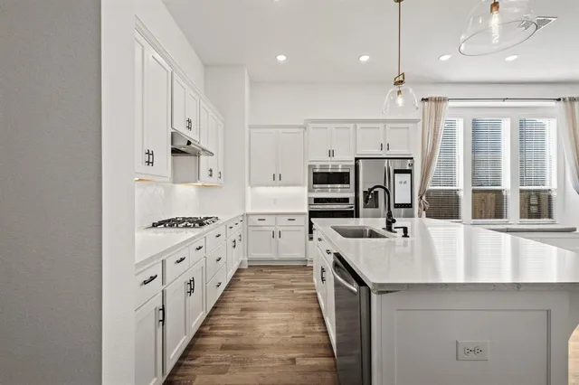 a kitchen with stainless steel appliances a refrigerator a sink dishwasher a stove and white cabinets with wooden floor