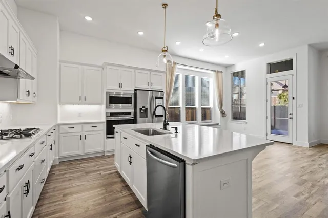 a kitchen with stainless steel appliances a refrigerator a sink dishwasher a stove and white cabinets with wooden floor