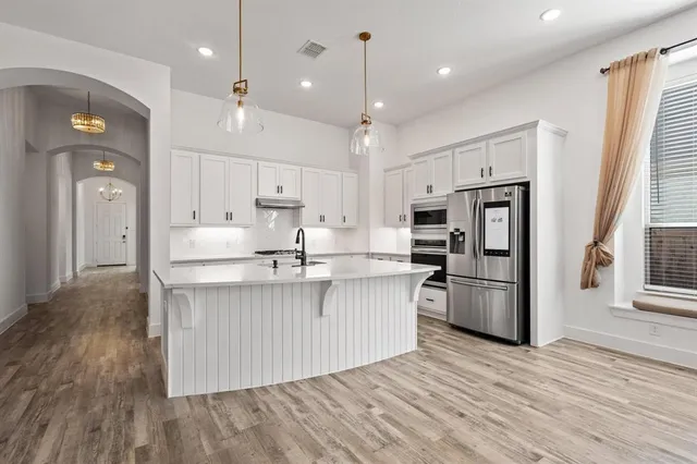 a large white kitchen with a sink a refrigerator and white cabinets