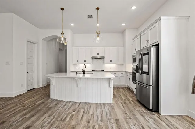 a large white kitchen with a stove a sink a center island and wooden floor
