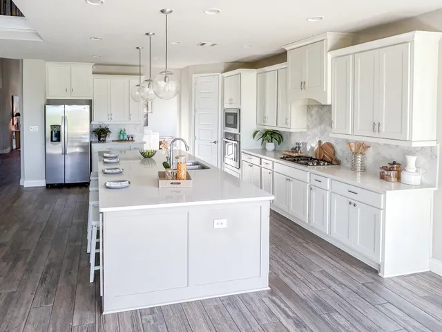 a kitchen with stainless steel appliances granite countertop a sink a stove a refrigerator and white cabinets with wooden floor