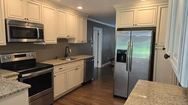 a kitchen with stainless steel appliances granite countertop a refrigerator a stove and a sink with wooden floor