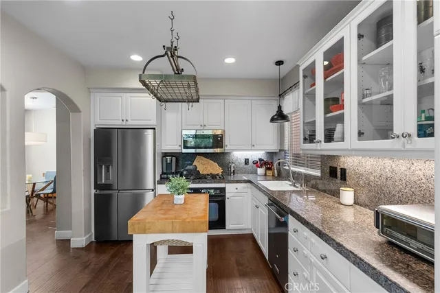 a kitchen with stainless steel appliances granite countertop a refrigerator a sink dishwasher a stove and a dining table with wooden floor