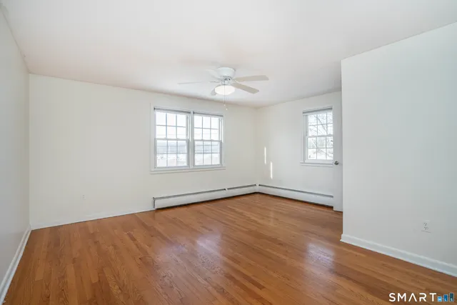 an empty room with wooden floor ceiling fan and windows