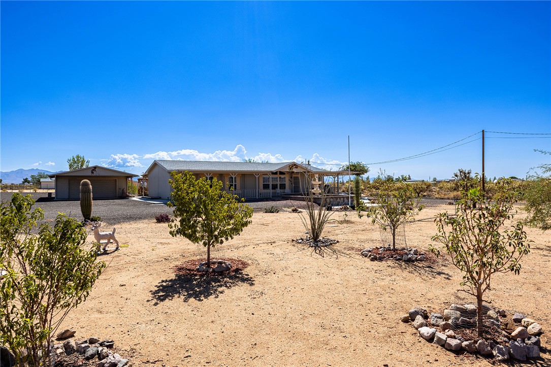 4206 Cordes Road Golden Valley, AZ 86413 - Photo 1 of 60 The property features a single-story residence with a covered front porch, a detached garage, and an expansive yard with several young trees and desert landscaping