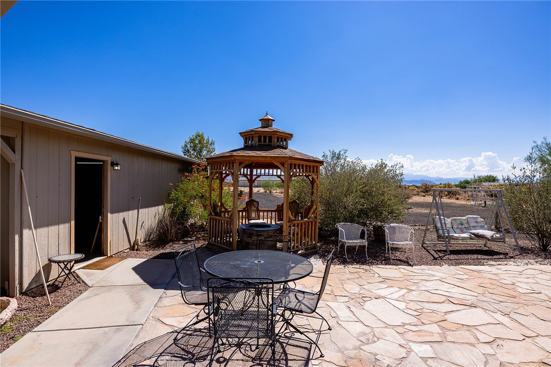4206 Cordes Road Golden Valley, AZ 86413 - Photo 33 of 60 The property features a spacious flagstone patio, a wooden gazebo, and a swing set, all set against a clear blue sky