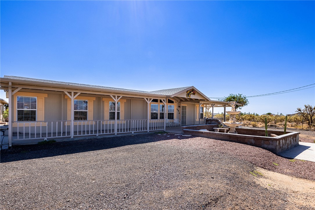 4206 Cordes Road Golden Valley, AZ 86413 - Photo 36 of 60 The property features an extensive covered porch, multiple windows with decorative shutters, and a decorative fountain with an adjacent stone-clad planter box