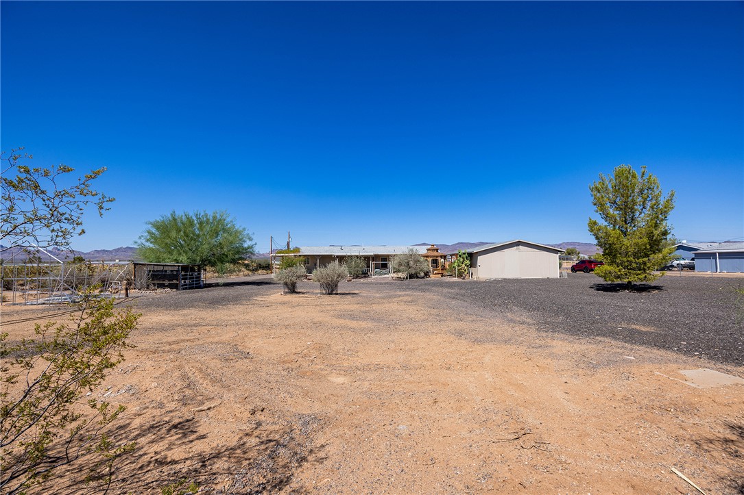 4206 Cordes Road Golden Valley, AZ 86413 - Photo 46 of 60 The property features an extensive lot with desert landscaping, including mature trees and shrubs, set against a clear blue sky