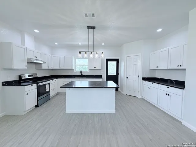 a large kitchen with stainless steel appliances a large stove a sink dishwasher a refrigerator and white cabinets with wooden floor