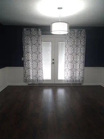 an empty room with wooden floor and windows with curtains
