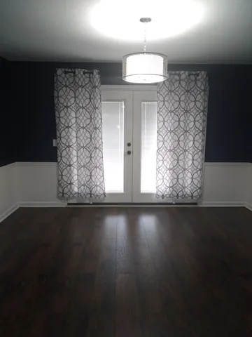 an empty room with wooden floor and windows with curtains