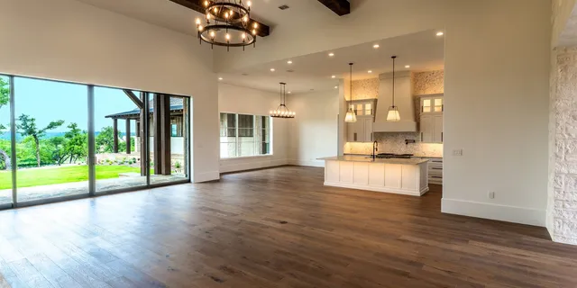 a view of an empty room with wooden floor and a kitchen