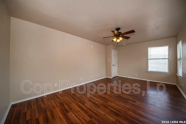 a view of an empty room with wooden floor and a ceiling fan