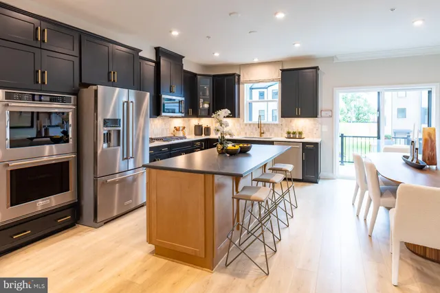 a kitchen with stainless steel appliances kitchen island granite countertop a refrigerator a stove top oven a sink dishwasher and white cabinets with wooden floor