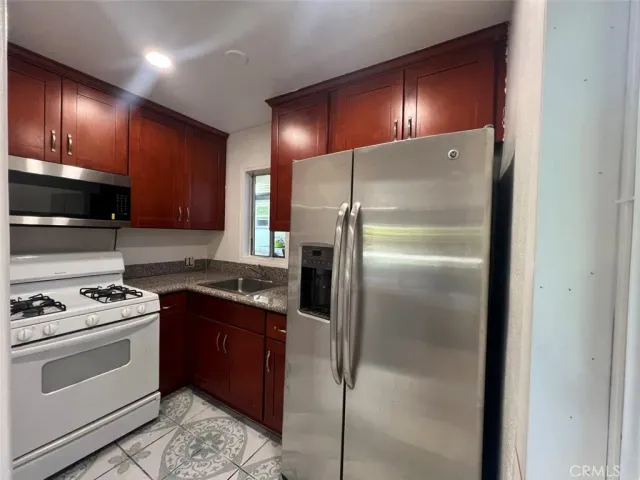 a kitchen with stainless steel appliances granite countertop a refrigerator a stove and a sink with wooden floor